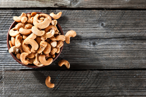 Raw cashew nuts in bowl on textured wooden background, table top view, selective focus photo