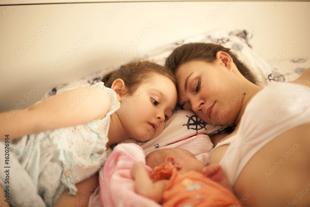 Happy Mother Laying in Bed with Daughter and Newborn Baby Happy Mother Laying in Bed with Daughter and Newborn Baby
