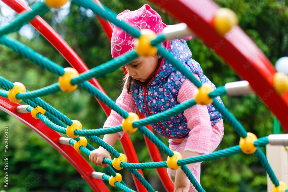 Portrait of Happy little blond girl playing on a rope web playground outdoor