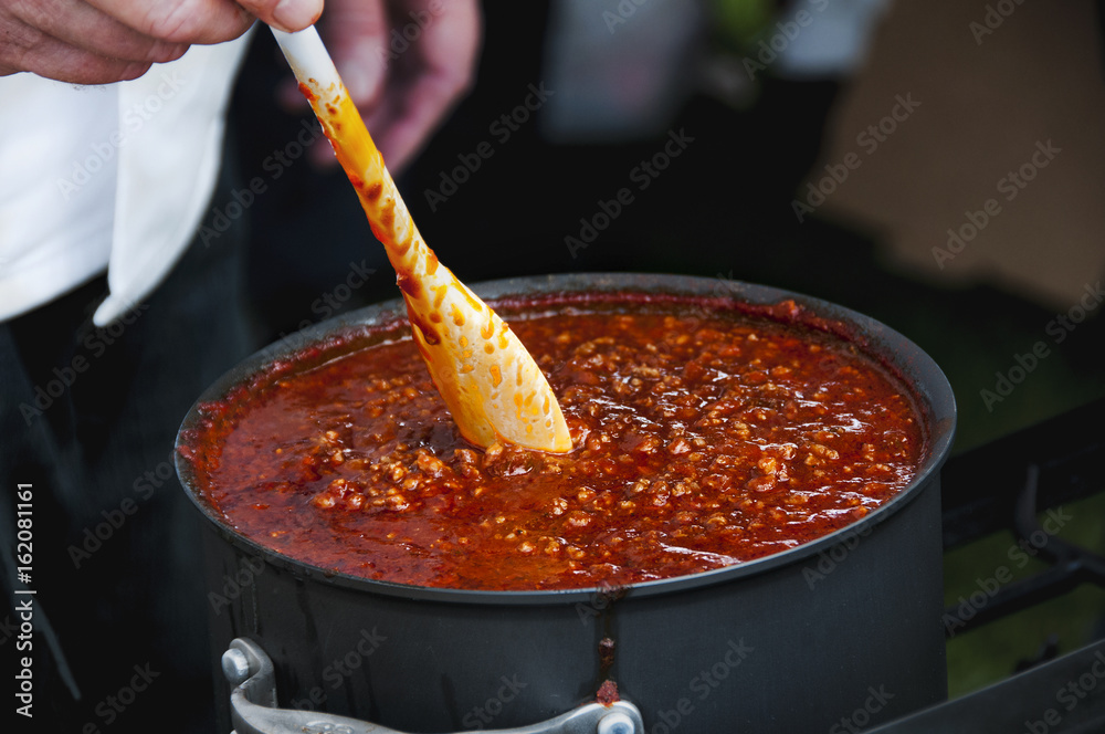 Cook Stirring a Simmering Pot of Spicy Chili - obrazy, fototapety, plakaty 