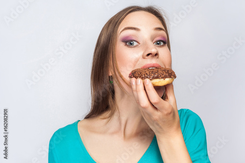 Portrait of beautiful girl with chocolate donuts. eating and looking at camera. studio shot on light gray background.