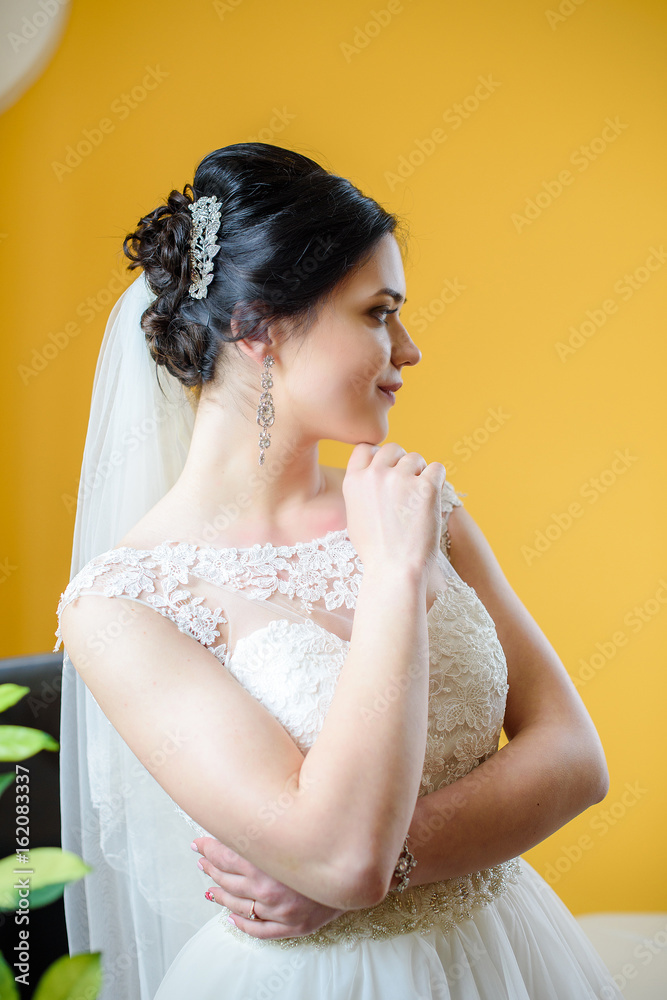 Beautiful bride perfect style. Wedding hairstyle make-up luxury wedding dress. Young attractive multi-racial Asian Caucasian model like a bride isolated on yellow background smells. Wedding