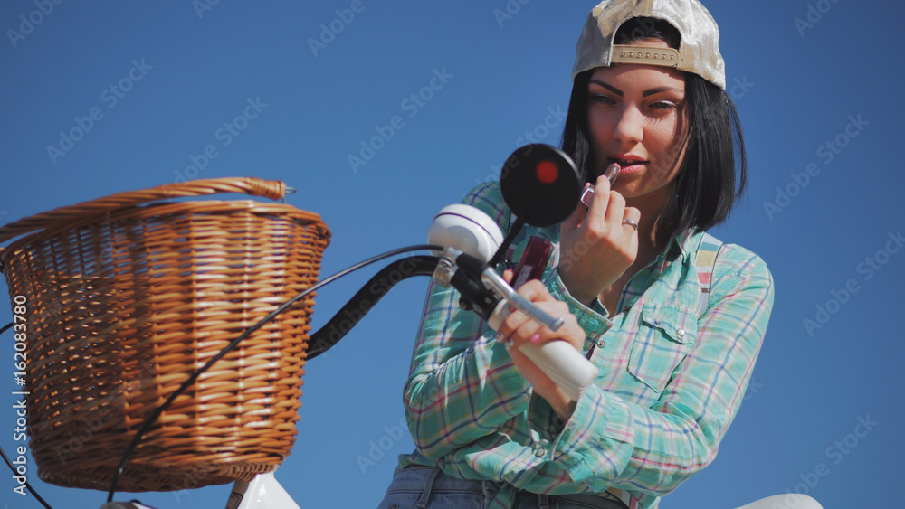 Woman is painting lipstick, woman with lipstick, woman is looking in bicycle mirror - obrazy, fototapety, plakaty 