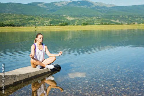 Teenage girl doing yoga outside in summer by the lake