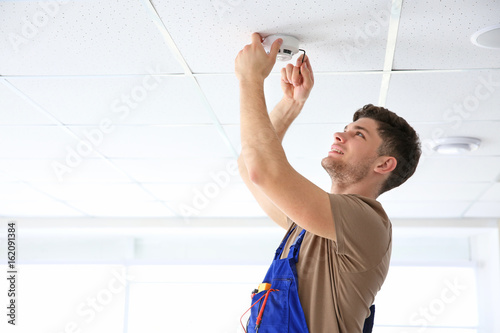 Young electrician installing smoke detector on ceiling