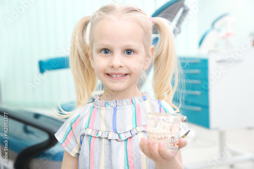 Cute little girl with plastic jaw mockup at dentist's office