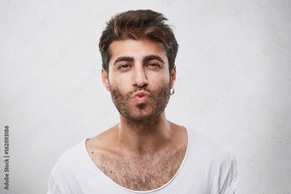 Lovely handsome guy flirting with girl blowing her kiss. Unshaved man with attractive appearance showing to his girlfriend sympathy going to kiss her. Macho man isolated over white background