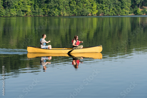 Couple paddling in yellow canoe on tree lined lake photo