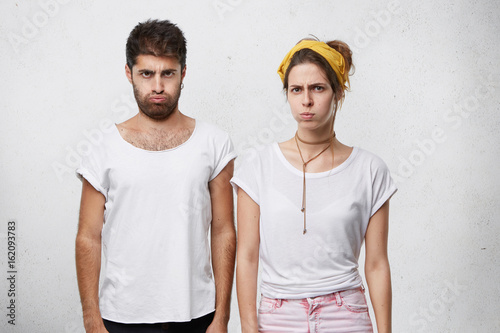 Young angry couple having sulky expressions blowing their cheeks with despair having bad relationships after quarrel. Young pretty female being angry with her husband. Couple having conflict