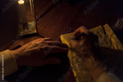 A grandfather writes a letter under candlelight on old, wrinkled paper. 