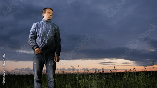 A cute young man waves off mosquitoes at sunset on the field. Beautiful sky on a background. photo