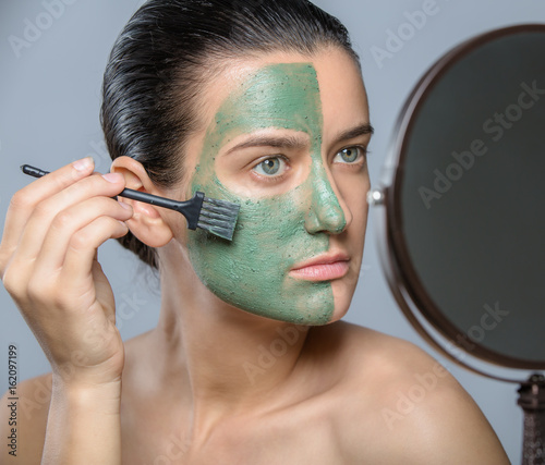 Young woman applaying green face mask - studio portrait photo