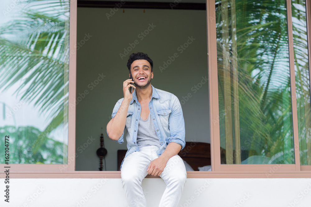 Fototapeta premium Young Hispanic Man Talking Phone Call Tropical Forest Hotel Terrace Holiday Guy Summer Vacation Travel