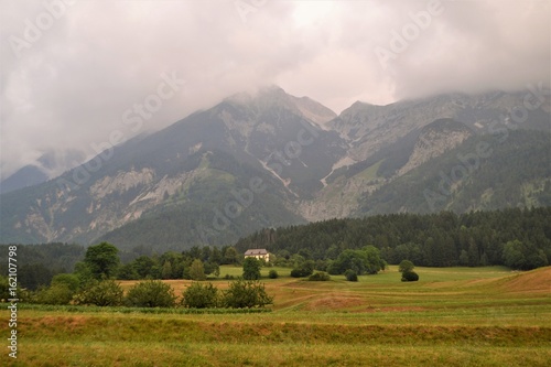 Felder mit Wald und bewölkter Berglandschaft