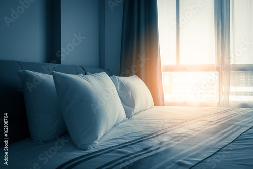 Bed maid-up with clean white pillows and bed sheets in beauty room. Close-up. Lens flair in sunlight.