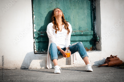 Beautiful modern resting woman holding cup orange juice, outdoor on street lifestyle, warmly, daytime