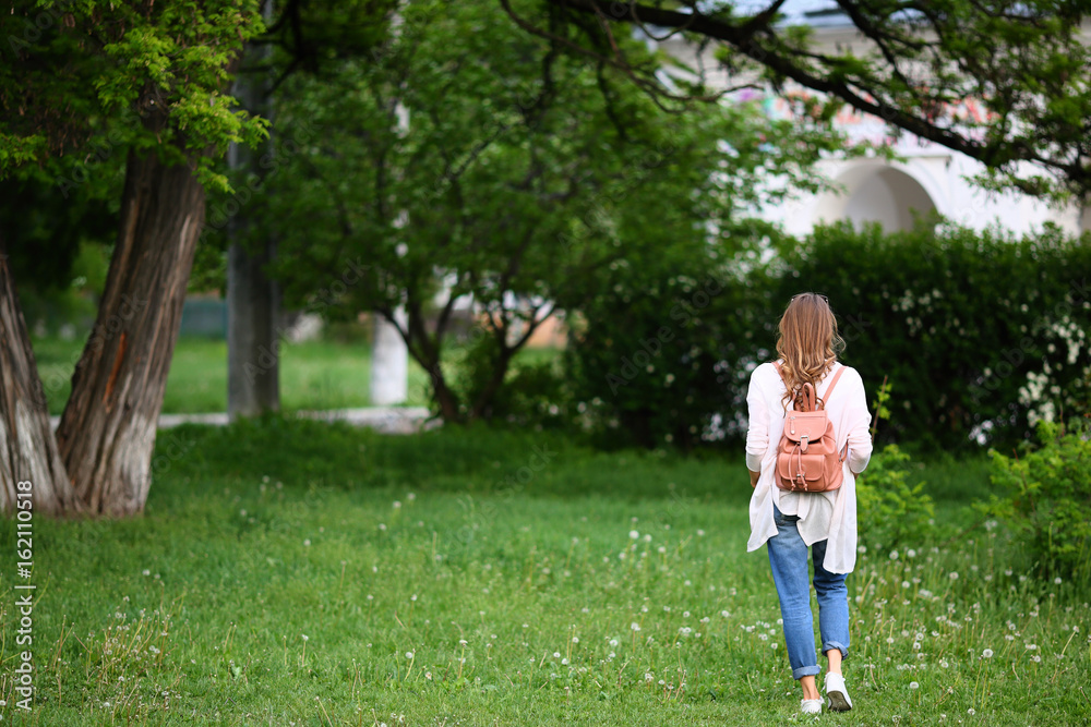 Young stylish woman standing back, casual clothes, in green park, outdoor, grass, full length Young stylish woman standing back, casual clothes, in green park, outdoor, grass, full length
