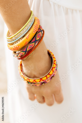 Close up of a woman hand with lot of bracelet, wristband, band, bangle, armlet on white summer skirt. Beauty cute girl on a tropical beach sea ocean shore with large stones. Outdoor summer lifestyle.