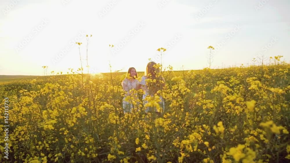 Two happy girls spinning in circles in the rape field with waving hair