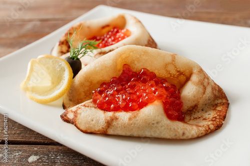 Luxury pancakes with red caviar with lemon. Russian traditional salty crepes with seafood. Shrove tuesday holiday food photo