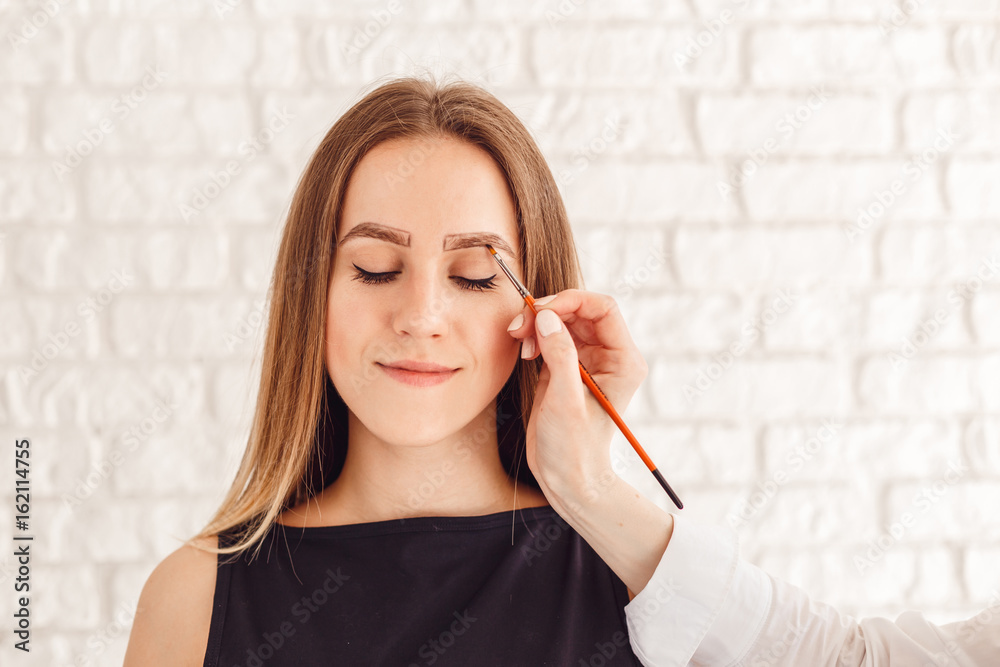 Eyebrow correction procedure for the smiling model with long eyelashes. Beautiful young woman gets eyebrow correction procedure. Eyebrow correction procedure for the smiling model with long eyelashes. Beautiful young woman gets eyebrow correction procedure.