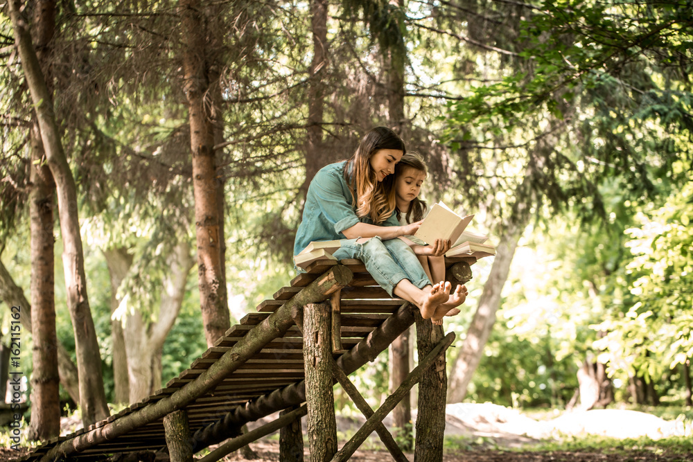 mother and daughter read a book in the park mother and daughter read a book in the park