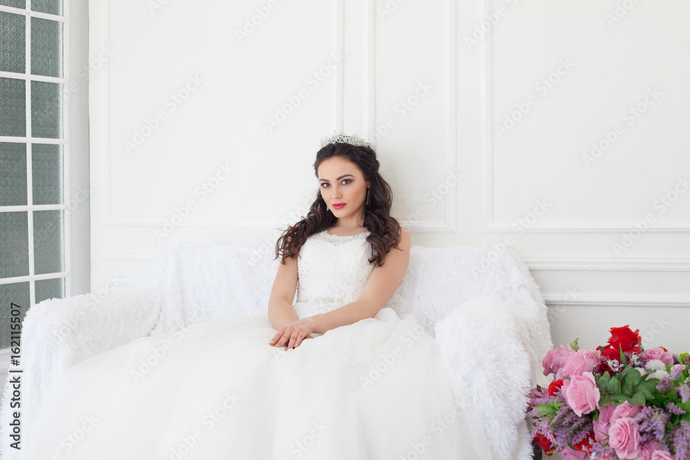 bride in a wedding dress and a crown sits in the white hall bride in a wedding dress and a crown sits in the white hall