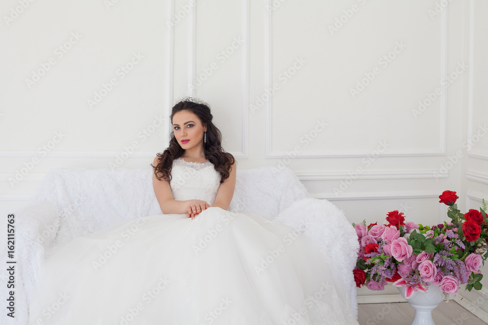 bride in a wedding dress and a crown sits in the white hall bride in a wedding dress and a crown sits in the white hall