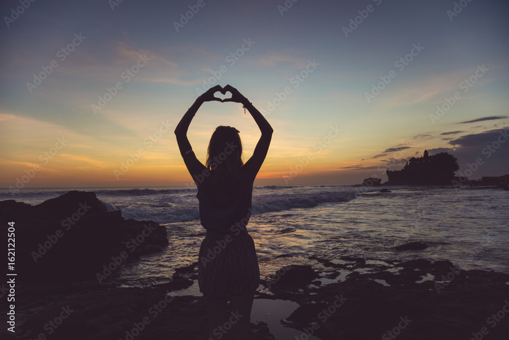 Girl holding a heart shape on the ocean / sea shore.
