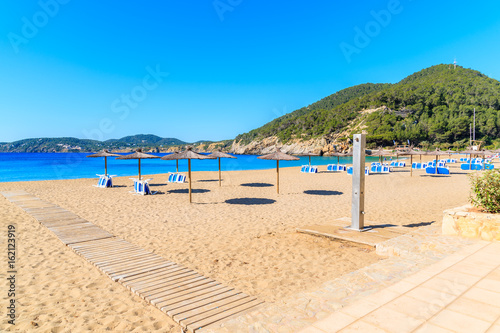 Sandy beach with umbrellas and sunbeds in Cala San Vicente bay on sunny summer day  Ibiza island  Spain