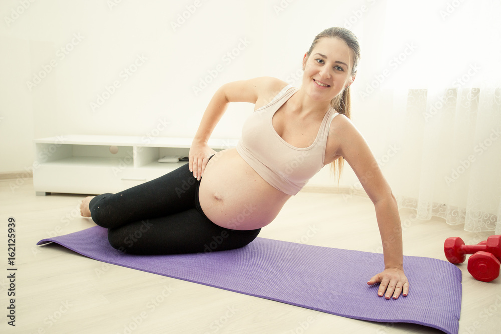 Smiling pregnant woman exercising on fitness mat at home
