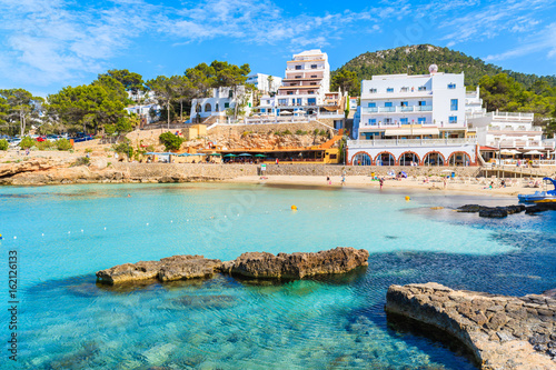 Hotel and restaurant buildings in Cala Portinatx bay with azure blue sea water, Ibiza island, Spain photo