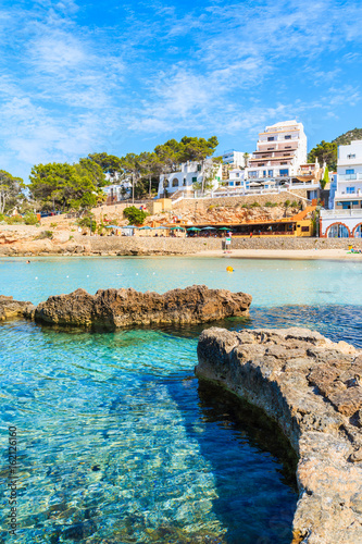 Hotel and restaurant buildings in Cala Portinatx bay with azure blue sea water, Ibiza island, Spain