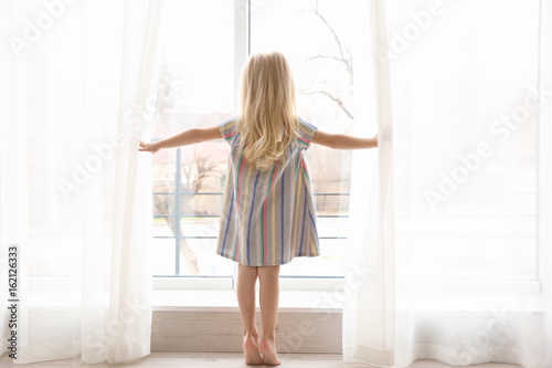 Small girl opening curtains