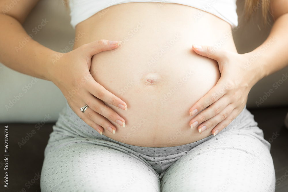 Closeup image of young pregnant woman holding hands on belly