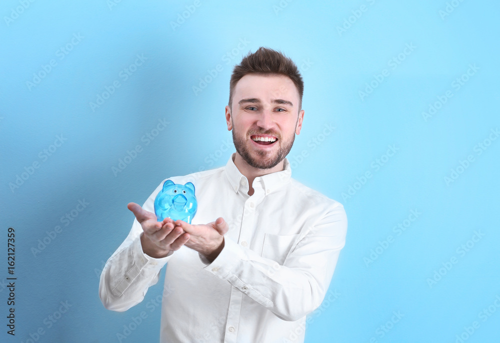 Happy young man holding piggy bank on light background Happy young man holding piggy bank on light background