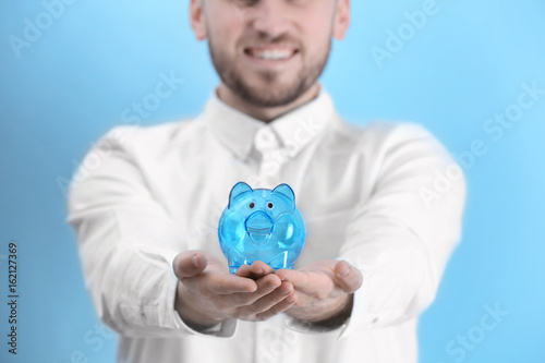 Happy young man holding piggy bank on light background