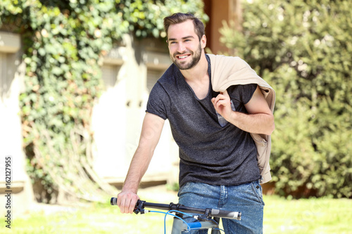 Handsome young man riding bicycle outdoors on sunny day © Africa Studio