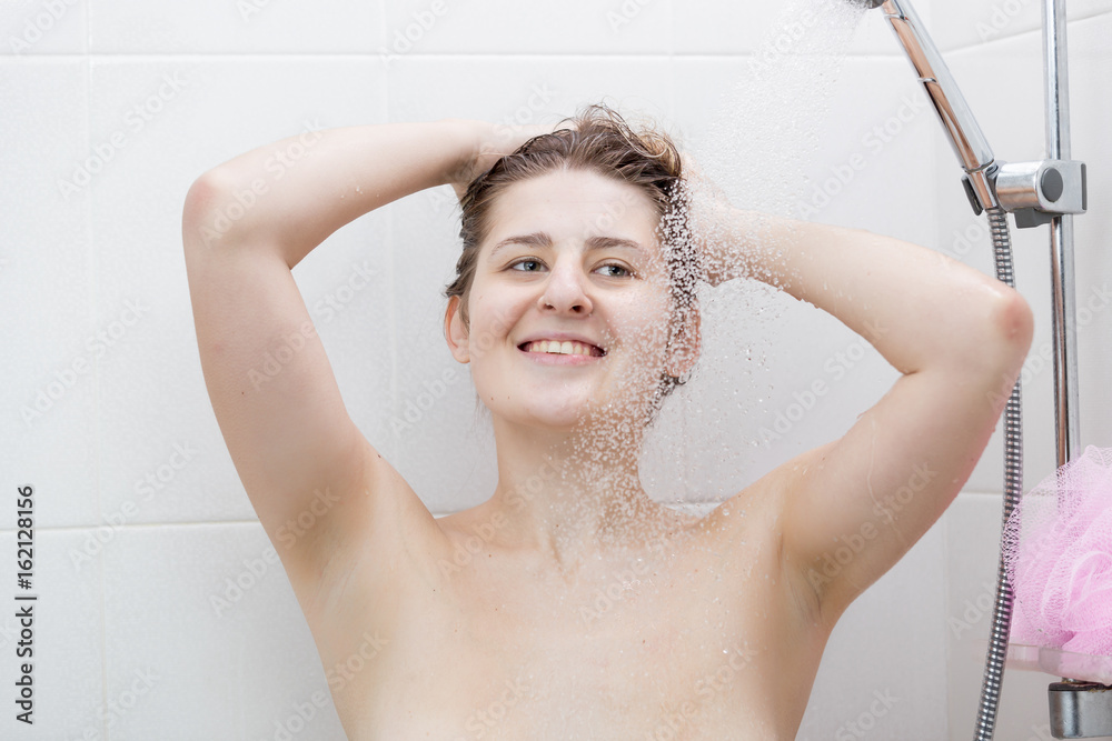 Naklejka premium Woman washing hair with shampoo at shower