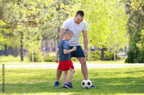 Father and son playing football on green grass in park © Africa Studio