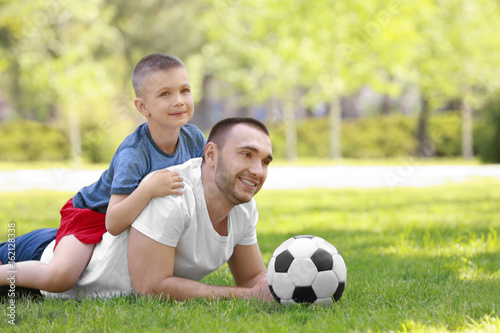 Father and son with soccer ball lying on green grass in park © Africa Studio