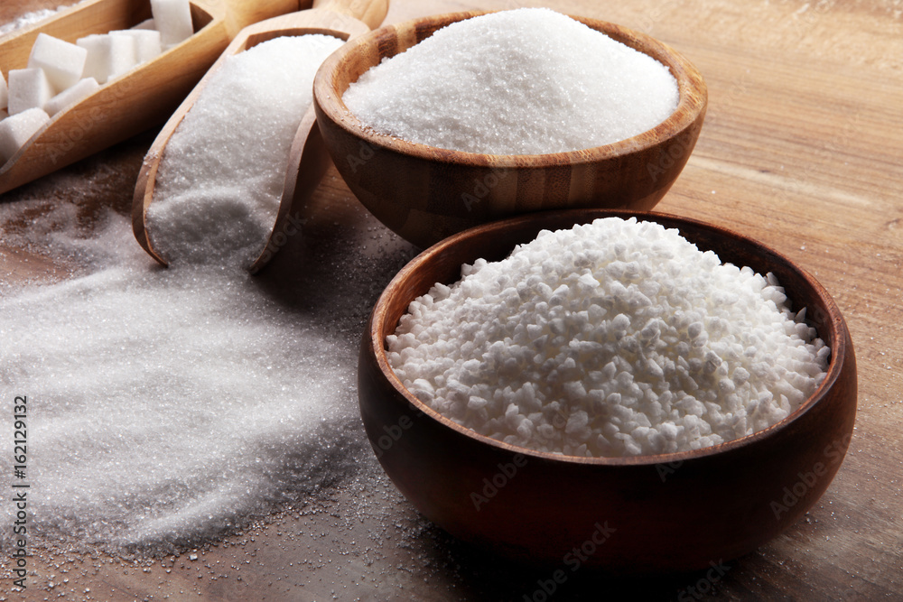 Bowl and scoop with white sand and lump sugar on brown wooden background Bowl and scoop with white sand and lump sugar on brown wooden background