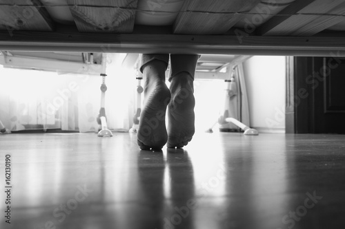 Black and white closeup photo of from under the bed on woman wearing slippers