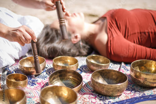 Woman playing a singing bowls also known as Tibetan Singing Bowls, Himalayan bowls. Making sound massage at beautiful sunny day.