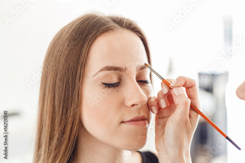 The master paints a new shape of the eyebrow to a client with a brush. Woman getting her eyebrows shaped at spa