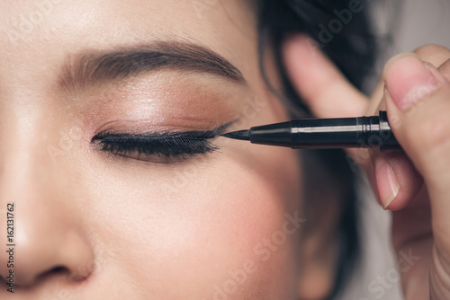 Close-up portrait of beautiful girl touching black mascara to her lashes photo