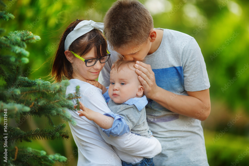 The underage family walks in the park with their little child. A young man gently kisses the baby on the top of the head The underage family walks in the park with their little child. A young man gently kisses the baby on the top of the head