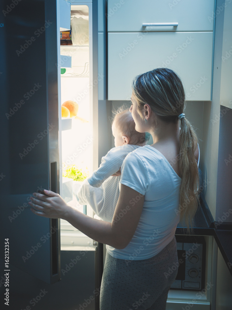 Mother with her baby opening refrigerator at late night Mother with her baby opening refrigerator at late night