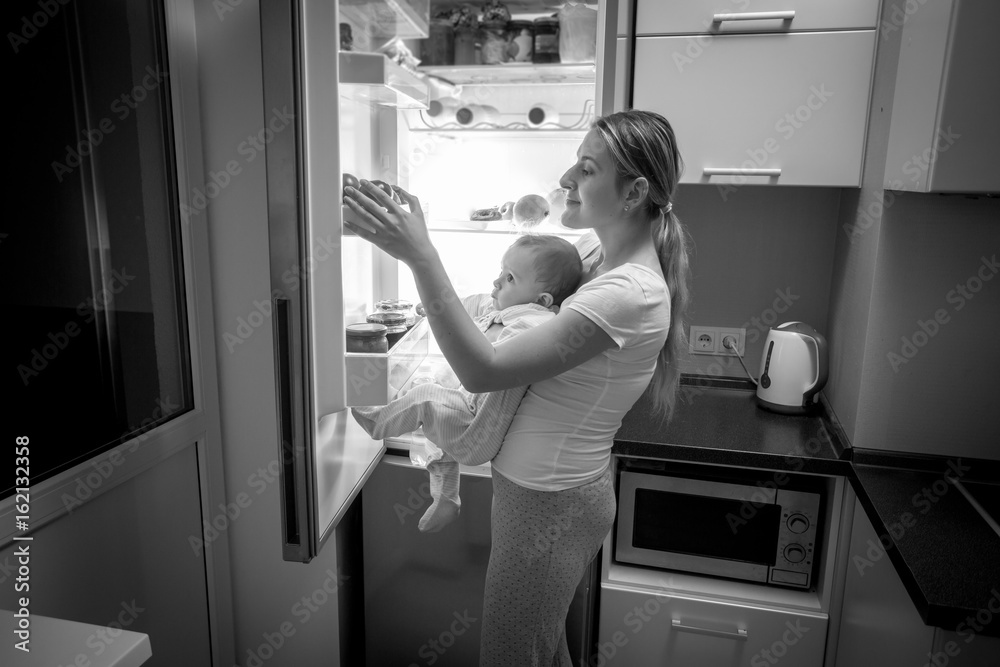 Black and white image of young mother and baby son looking inside the fridge for something to eat Black and white image of young mother and baby son looking inside the fridge for something to eat