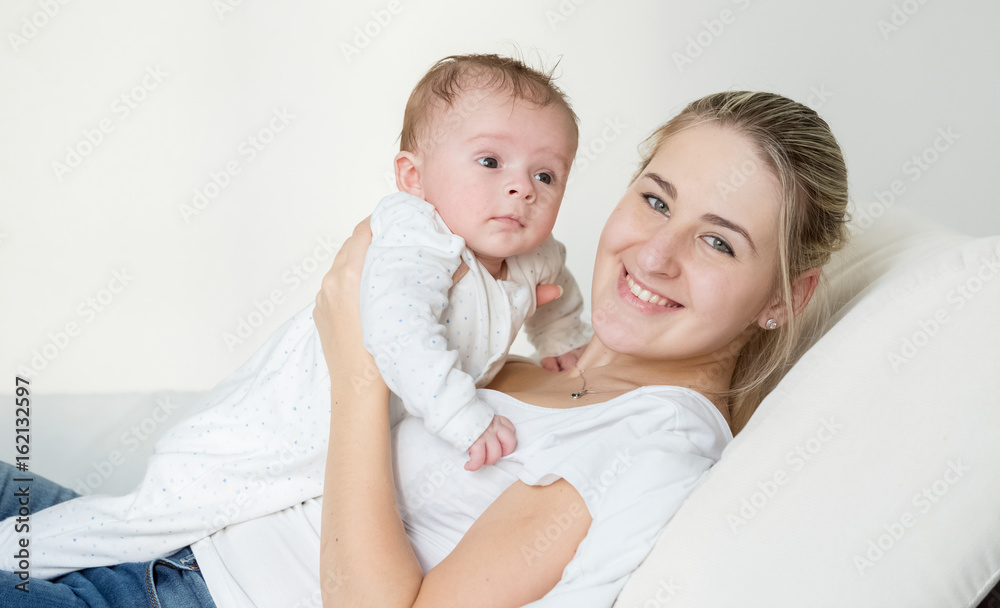 Portrait of beautiful smiling woman lying with her cute baby on pillow at bed Portrait of beautiful smiling woman lying with her cute baby on pillow at bed